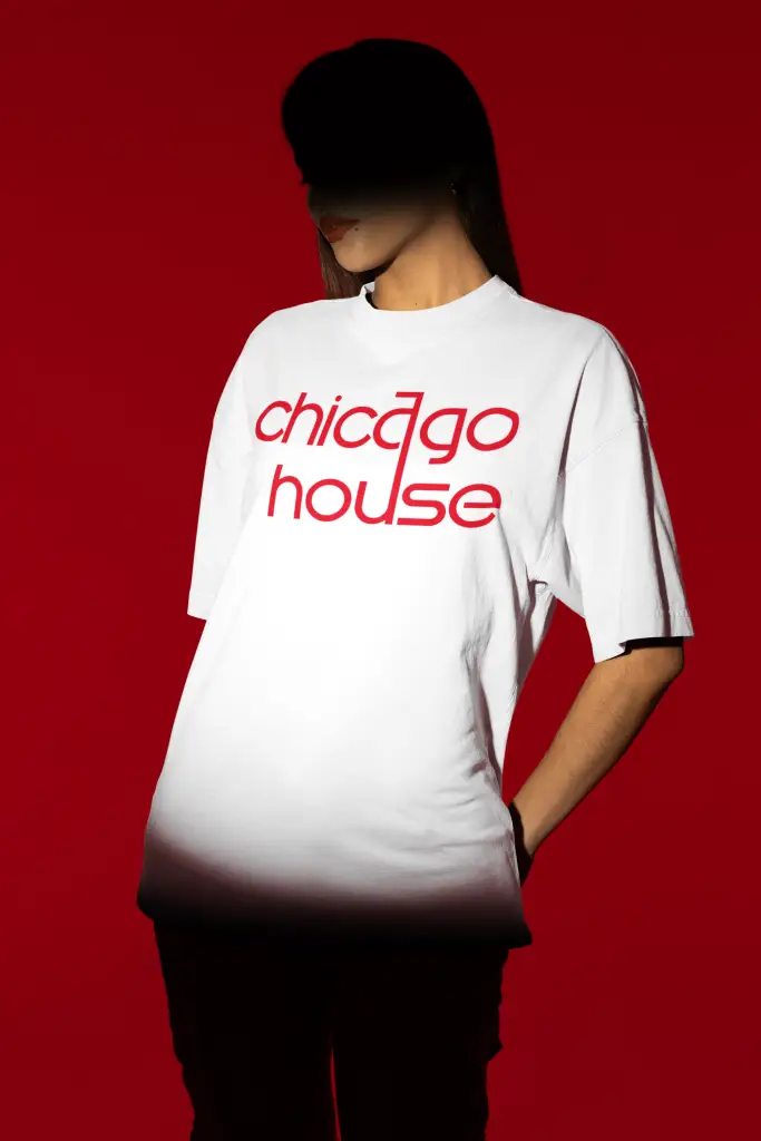 Person wearing a white crew neck t-shirt with red "chicago house" text graphic, under dramatic lighting with a red background.