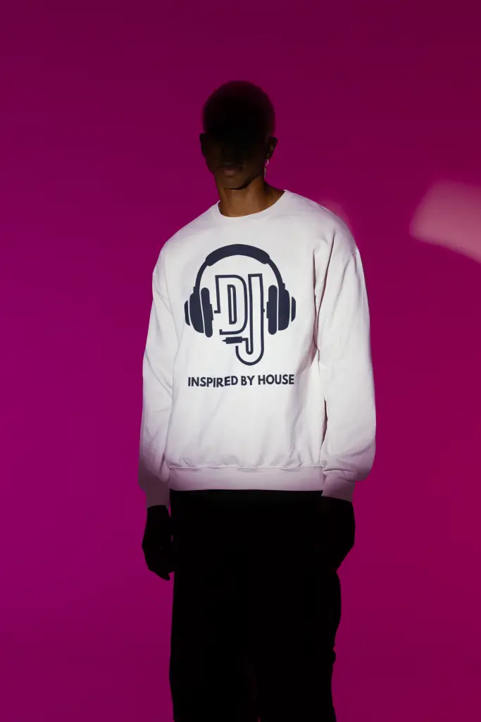 Person wearing a white sweatshirt with a black DJ headphones and "INSPIRED BY HOUSE" graphic, under dramatic pink and white lighting.